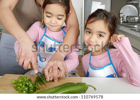 Twin sisters and mother chopping vegetables together on the kitchen counter at home.