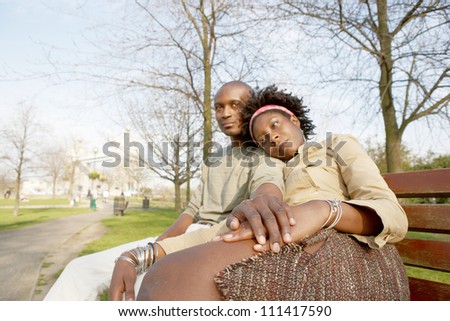 Young attractive black couple sitting down on a bench in the park while visiting the Tower of London, holding hands.