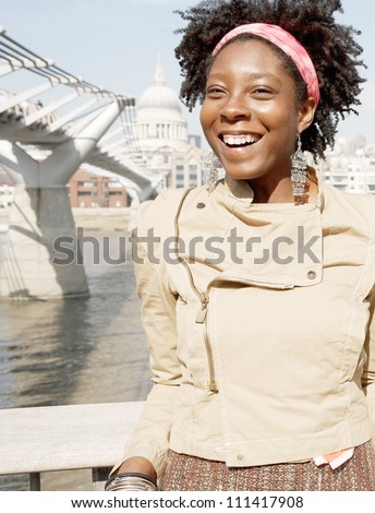 Portrait of a quirky black woman on vacations, visiting London city with the Millennium Bridge and St Paul\'s Cathedral behind her.