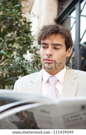Attractive young businessman reading the newspaper while sitting in the city near a classic office building.