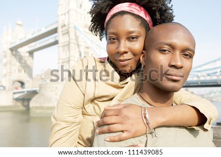 Portrait of an african american tourist couple visiting the Tower of London overlooking the river, hugging and smiling.