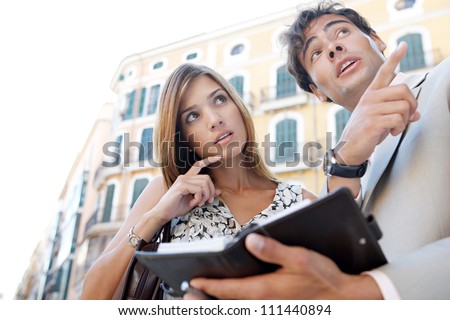 Businessman and businesswoman laughing while having a meeting outdoors, in a classic city, pointing in the same direction.