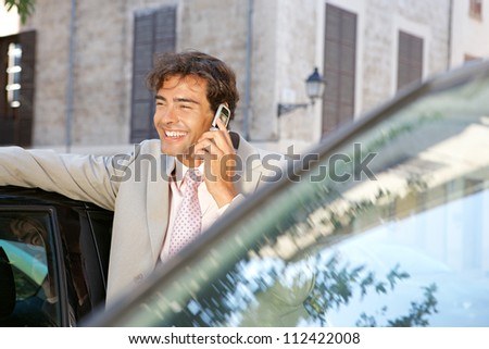 Businessman using a cell phone to make a phone call while standing some cars in the city, laughing.