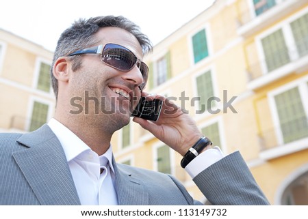 Close up portrait of a businessman having a phone conversation using his smart phone while standing in front of a classic building in the city, smiling.