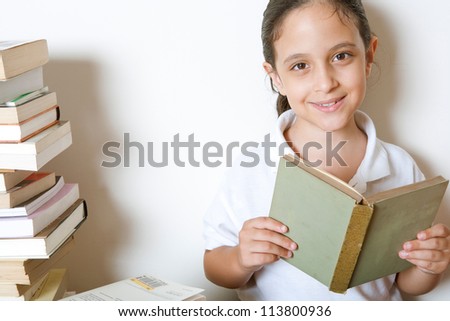 Close up of a young girl reading a book at home, sitting next to a pile of books.