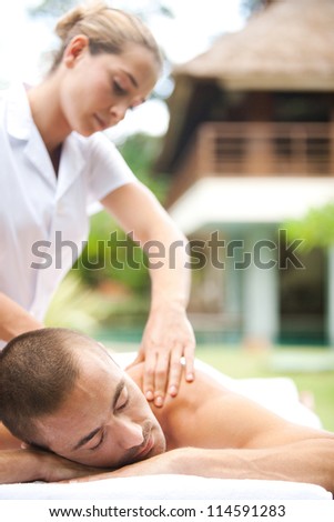 Young masseuse massaging an attractive man in a tropical hotel garden.
