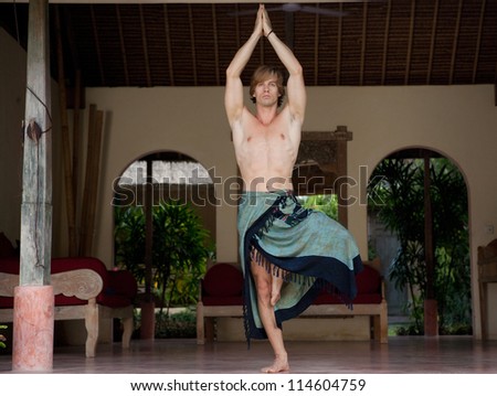 Attractive man doing yoga and keeping his balance while on a holiday villa\'s outdoor.