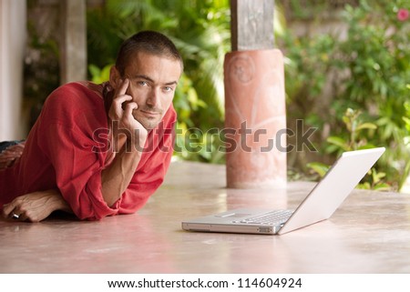 Attractive man using a laptop computer while laying down in a tropical garden on vacation.