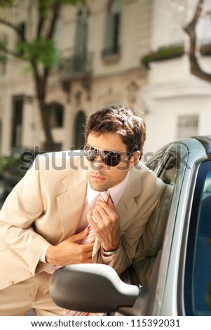 Attractive businessman grooming himself using a car mirror outdoors, tightening his tie knot.