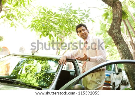 Young successful businessman with his car having a phone conversation using a hands free set in a tree lined street in the city.