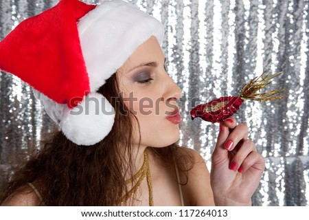 Attractive young woman kissing a christmas sequins bird while standing in front of a silver sequins background