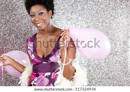 Attractive young black woman holding pink balloons against a silver glitter background, smiling.