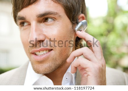 Close up portrait of an attractive young businessman using a hands free ear piece device to make a phone call while in a classic city financial district, outdoors.