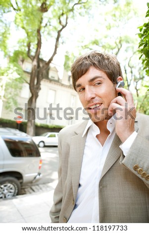 Attractive young businessman using a hands free ear piece device to make a phone call while in a classic city financial district, outdoors.