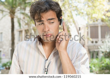 Young attractive businessman using a hands free device to have a conversation on his cell phone while standing in front of classic office buildings in the city.