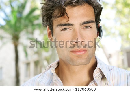 Close up portrait of an attractive businessman using a hands free device to make a phone call while standing near office buildings in a classic city.