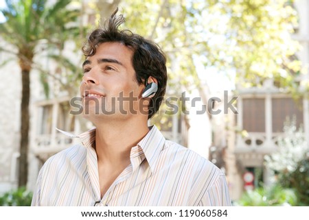 Young attractive businessman using a hands free device to have a conversation on his cell phone while standing in front of classic office buildings in the city.