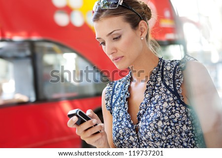 Portrait of an attractive commuting businesswoman using her smart phone in the city near a bus stop.