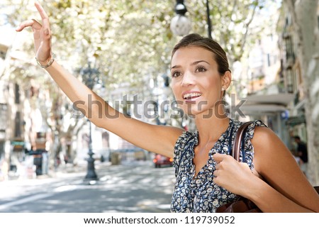 Attractive young businesswoman raising her arm to call a taxi in a busy city, outdoors.