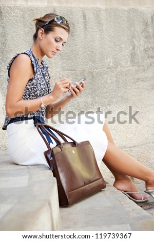 Attractive businesswoman sitting down on stone steps in the city, using a smart phone.