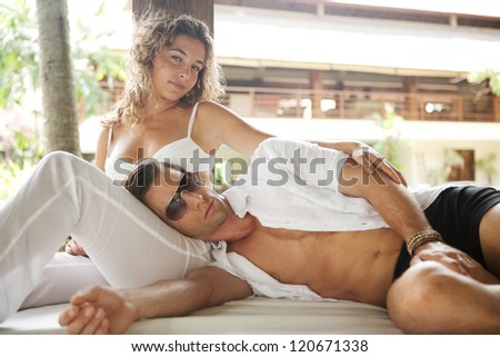 Young and attractive sexy couple lounging on a tropical garden bed in an exotic hotel spa garden, relaxing together.