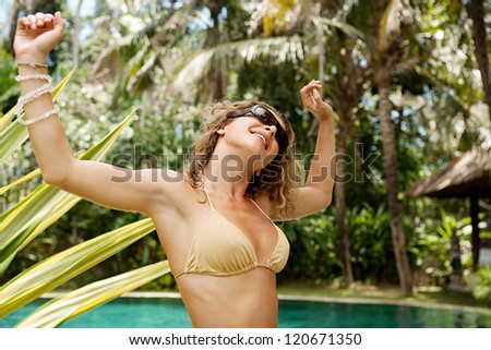 Beautiful and sexy young woman dancing in a golden bikini near a swimming pool in a topical garden during a sunny day on vacations.