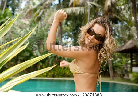 Beautiful and sexy young woman dancing in a golden bikini near a swimming pool in a topical garden during a sunny day on vacations.