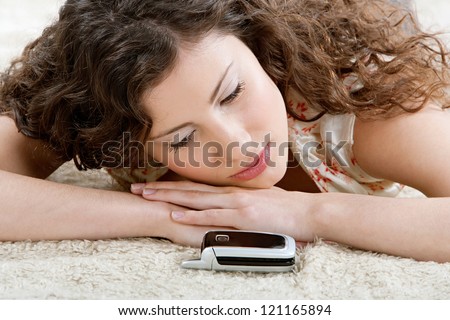 Beautiful young hispanic woman laying down on a furry carpet at home, looking at her cell phone and patiently waiting for a phone call.