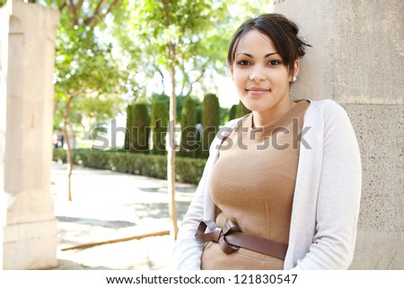 Close up portrait of an attractive young woman leaning on a column while visiting a botanic garden on a sunny day, smiling at the camera.