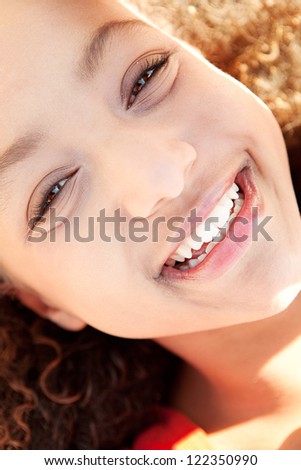 Over head close up portrait of a beautiful young girl laying down on a golden sand beach on a sunny day, smiling at the camera.