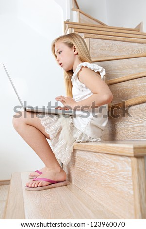 Profile view of a young girl child using a laptop computer while sitting down on her home\'s wooden steps.