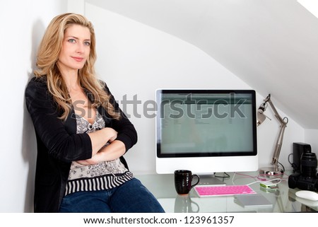 Portrait of an attractive professional woman sitting on her work desk being proud and successful, next to her computer screen.