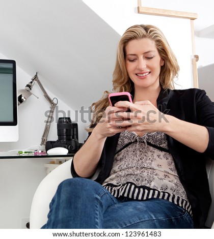 Attractive businesswoman working from home office and using a smart phone while working at her desk.