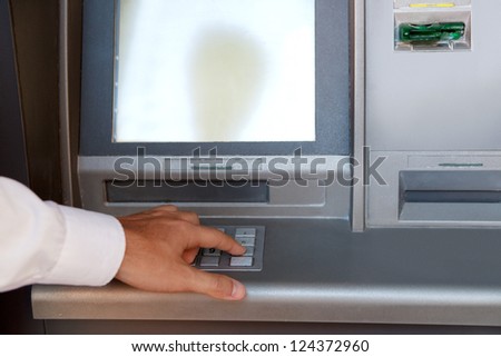 Businessman hand pressing a key in the keypad of a cash machine, outdoors.