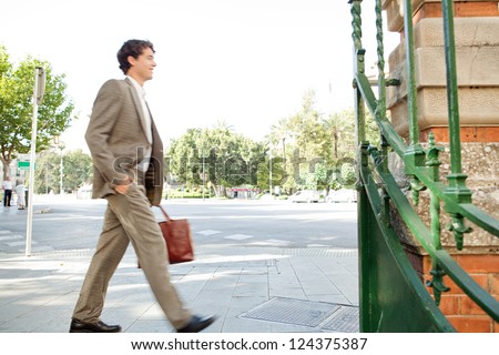 Suited businessman walking fast through the city on his way to work and carrying a briefcase, outdoors.