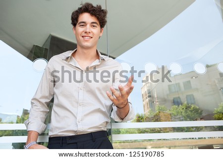 Graphic portrait of a confident businessman gesturing with his hand while talking to the camera next to a building window with reflections of the city.