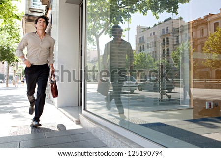 Attractive young businessman running though the city being late for work.
