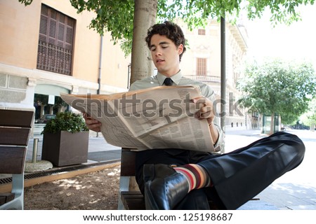 Young businessman reading a financial newspaper while sitting on a bench in the city, wearing quirky and colorful stripy socks.