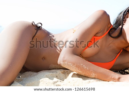 Middle section view of a sexy woman body laying down on a white sand beach, relaxing while on vacation against a blue sky.