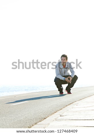 Sports man crouching down on running track by the sea, with a blue sky in the background, on a sunny day.