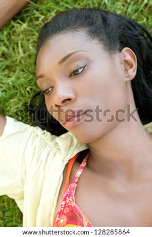 Over head close up portrait of an attractive african american woman laying down on green grass, outdoors.