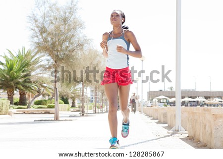 Attractive african-american woman running and exercising in the city, listening to music with her ear phones on a sunny day.