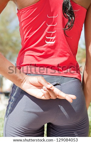 Close up rear view of a black woman standing after exercising, keeping her fingers crossed behind her back for good luck.