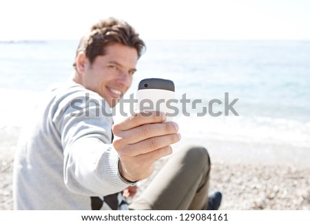 Smart man sitting down on a pebble beach, turning around to take a picture with his \
