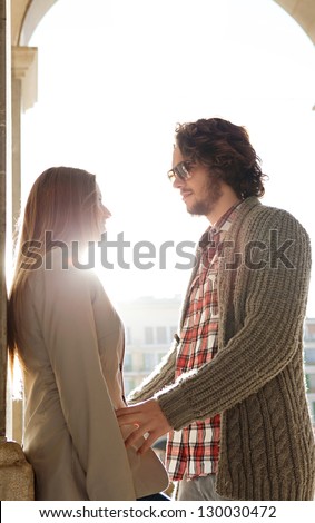 Profile view of a young tourist couple being romantic under an old city arch with the sun rays filtering through, while on vacation.