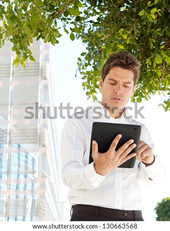 Portrait view of a successful businessman using a digital tablet pad while standing by a modern office building in the financial city, outdoors.