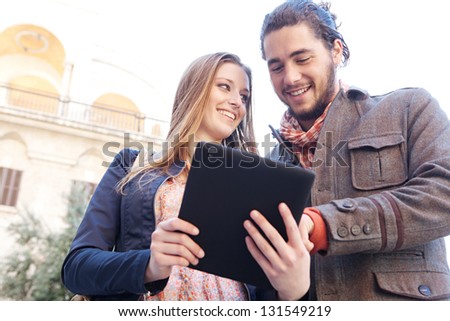 Young tourist couple standing together in a destination city holding and sharing a digital tablet pad while on vacation, smiling.