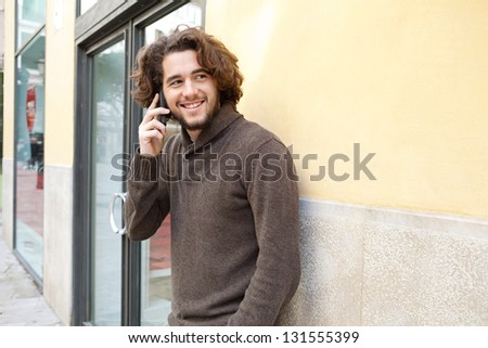 Portrait of a young man using a cell phone to make a call while standing by an office building entrance, outdoors.