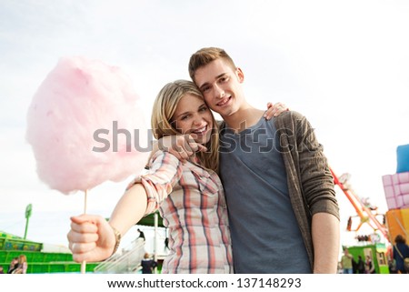Portrait of a young couple in a colorful attractions park with rides holding a cotton candy sugar sweet, having fun.