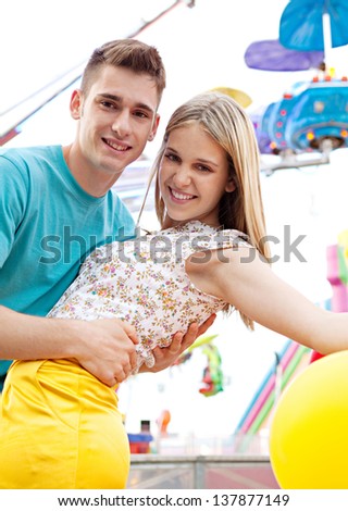 Close up of a young couple visiting fun fair park arcade being romantic during an early evening with lights and rides in the background.